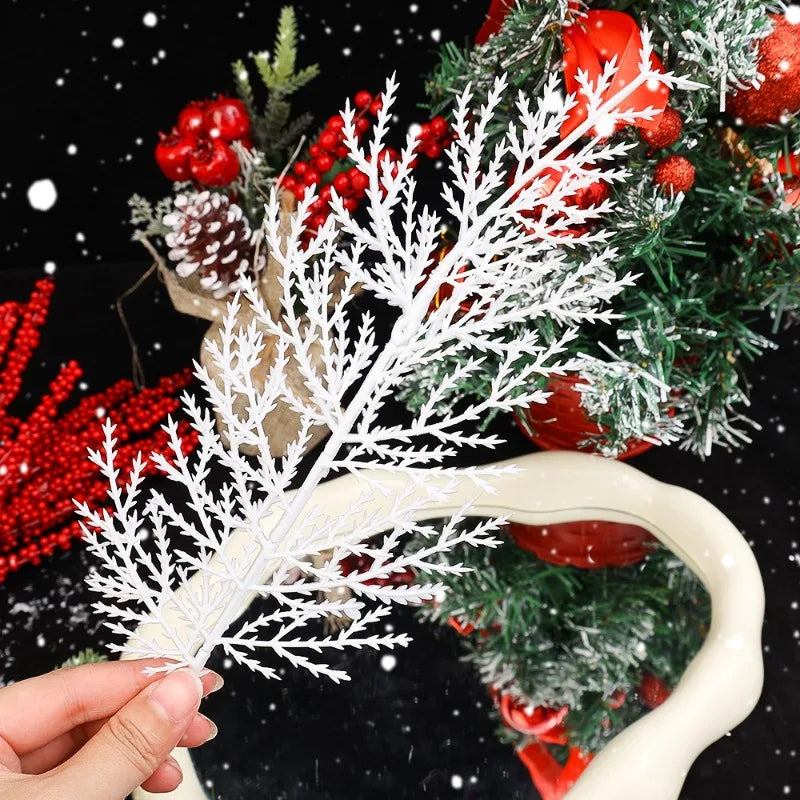 White decorative branch held by a hand with a Christmas tree in the background
