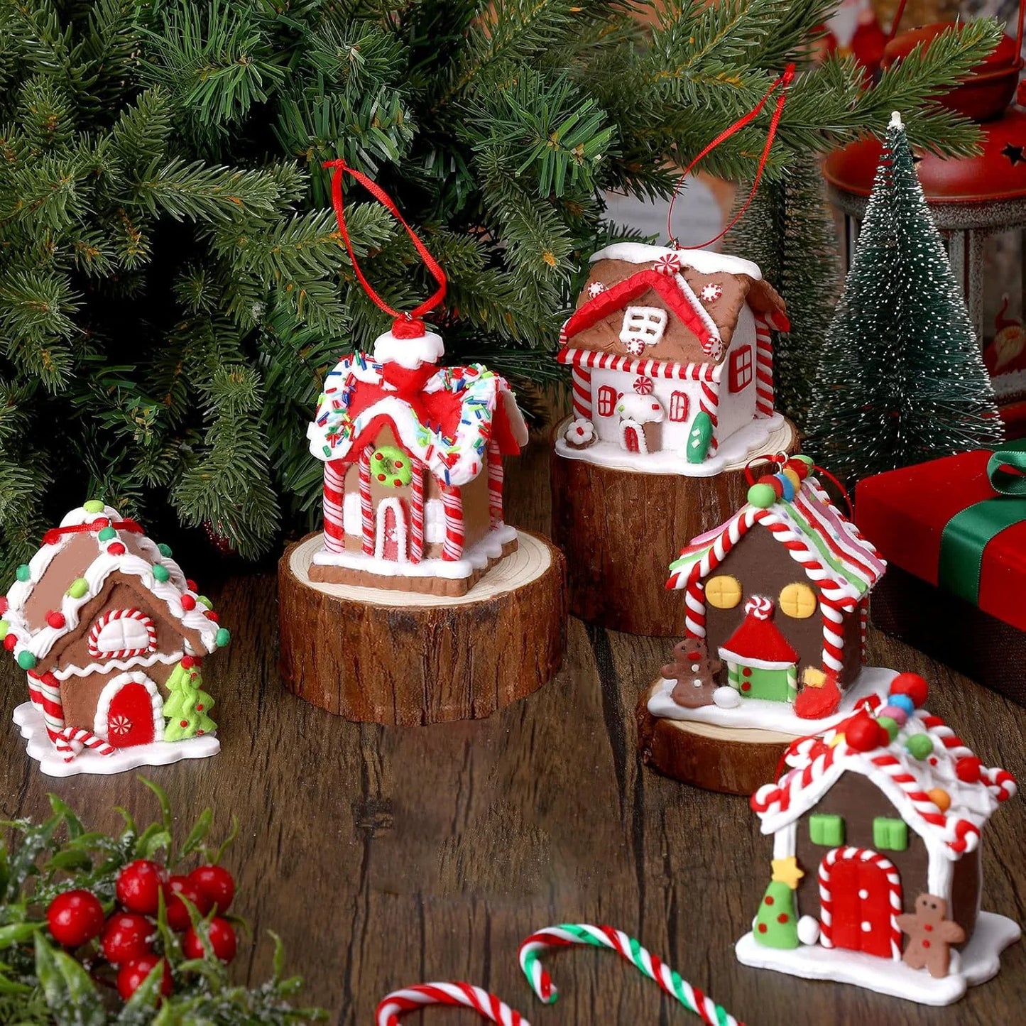 Decorative gingerbread house ornaments on a wooden surface with a Christmas tree in the background.