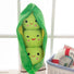 Plush toy shaped like a green pea pod with three smiling peas inside, on a white surface.