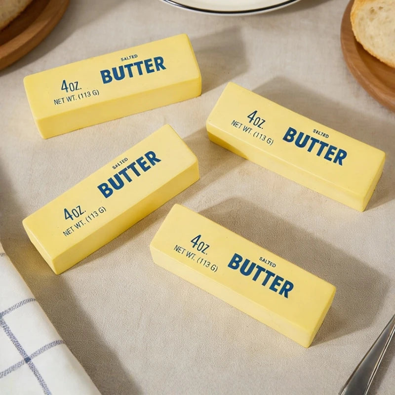 Four blocks of butter on a kitchen counter with a cloth and bread in the background.