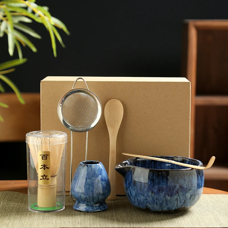 Tea-making set with blue ceramic pot, wooden spoon, metal strainer, and transparent container on a dark background.