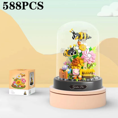 Toy garden set with bees and flowers inside a glass dome on a white surface.