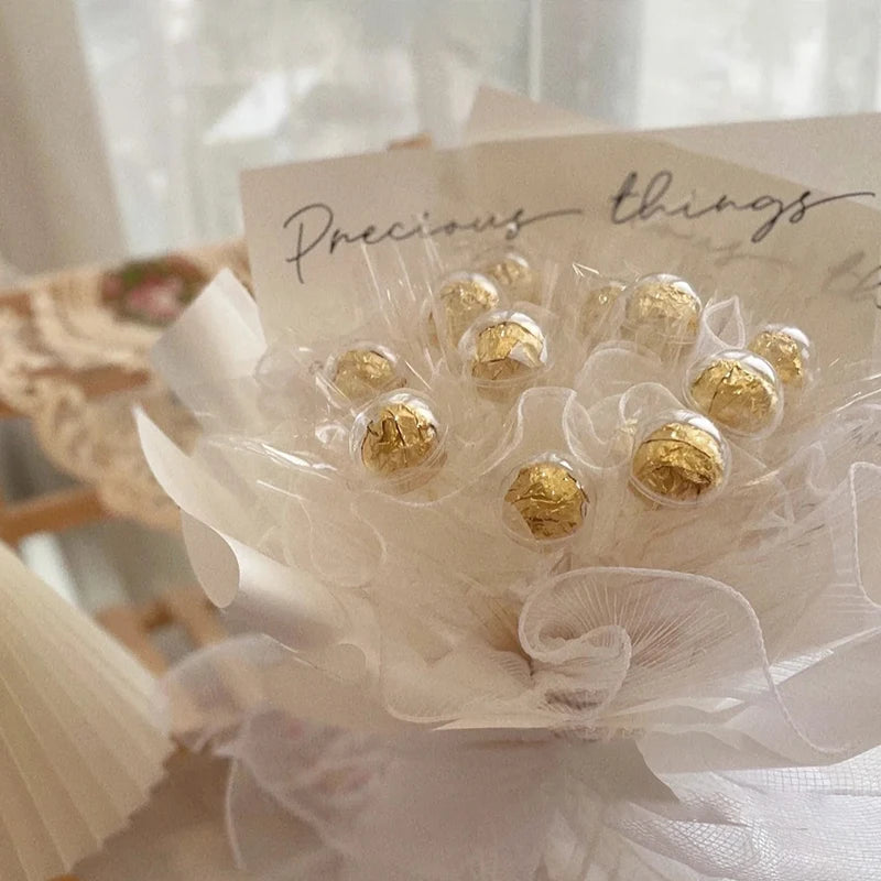 Bouquet of gold-wrapped candies with white ribbons on a light background