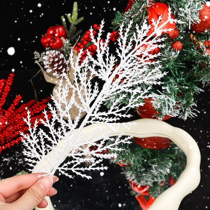 White decorative branch held by a hand with a Christmas tree in the background