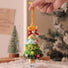 Handmade crocheted Christmas tree ornament with colorful decorations, held by a hand against a blurred indoor background.