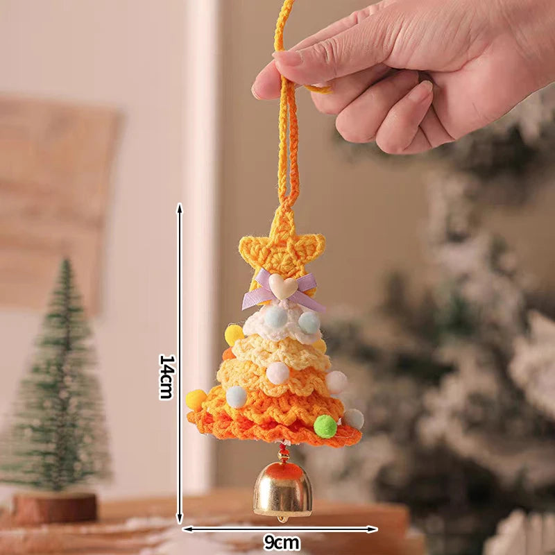 Hand holding a colorful crocheted bell with measurements indicated, against a blurred indoor background.