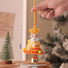 Hand holding a colorful crocheted bell with measurements indicated, against a blurred indoor background.
