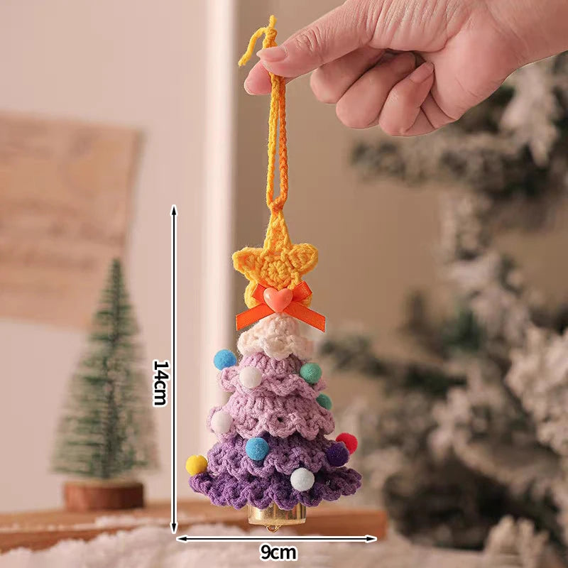 Hand holding a small crocheted Christmas tree ornament with measurements, blurred Christmas tree in the background