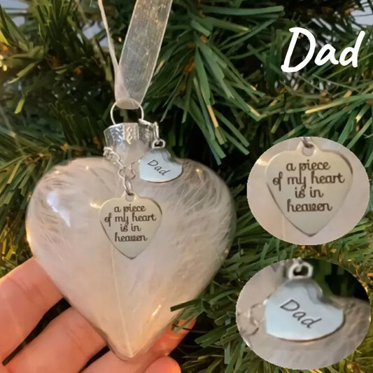 Heart-shaped ornament with 'Dad' and 'a piece of my heart is in heaven' tags, held against a Christmas tree background.