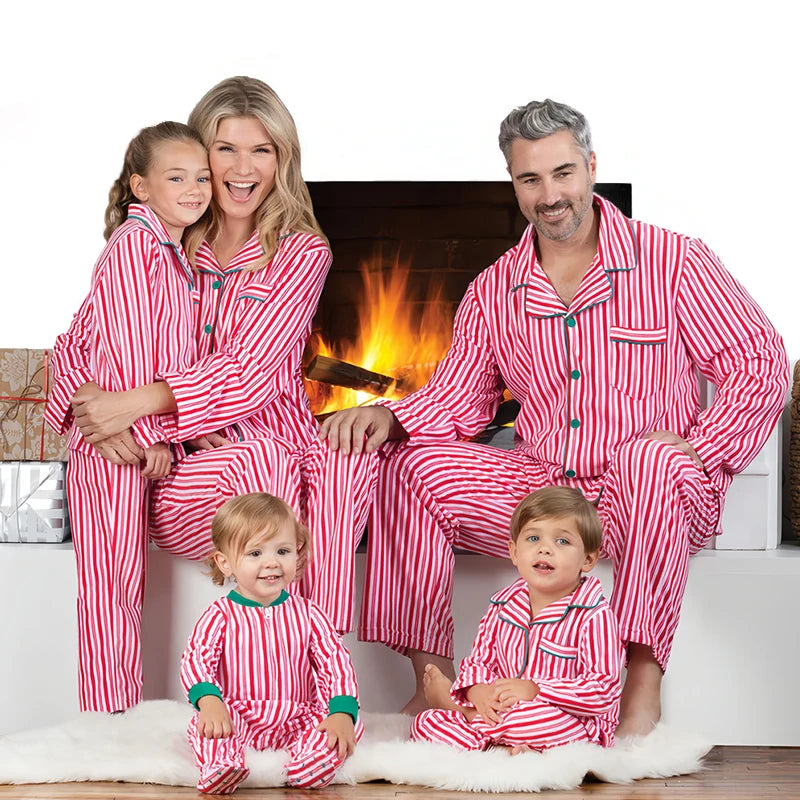 Family of five wearing matching red and white striped pajamas sitting in front of a fireplace.