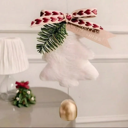 A fluffy white Christmas ornament shaped like a bell with a gold-colored hanging weight, decorated with a green pine branch and a pink ribbon with red hearts. A beige paper tag with 'Merry Christmas!' is attached.