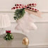 A fluffy white Christmas ornament shaped like a bell with a gold-colored hanging weight, decorated with a green pine branch and a pink ribbon with red hearts. A beige paper tag with 'Merry Christmas!' is attached.