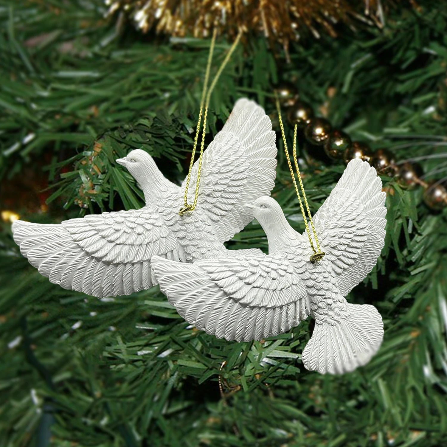 White dove Christmas ornaments on a green tree with gold decorations.