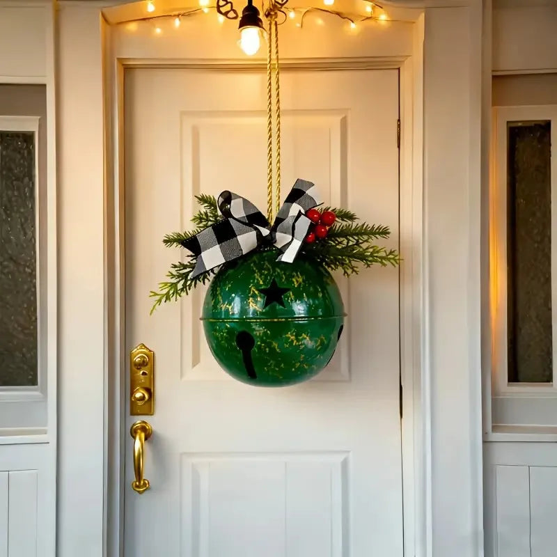 A green hanging Christmas ornament with a gold star, decorated with pine branches, red berries, and a black-and-white checkered bow, suspended in front of a white front door.