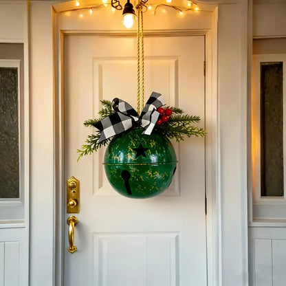 A green hanging Christmas ornament with a gold star, decorated with pine branches, red berries, and a black-and-white checkered bow, suspended in front of a white front door.