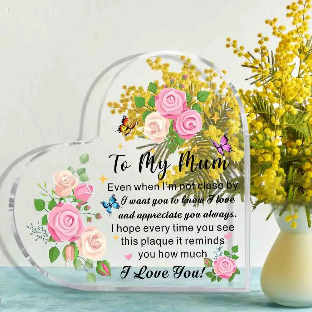 Heart-shaped plaque with floral design and message to 'My Mum' next to a vase of yellow flowers.