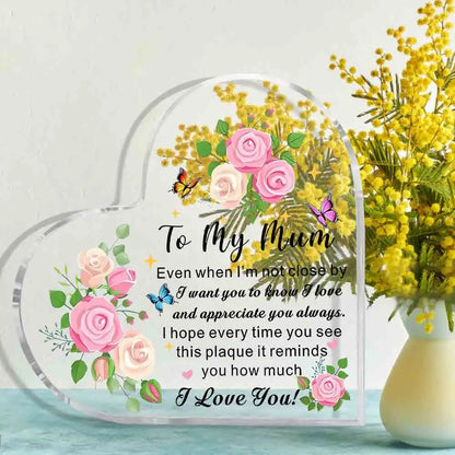Heart-shaped plaque with floral design and message to 'My Mum' next to a vase of yellow flowers.