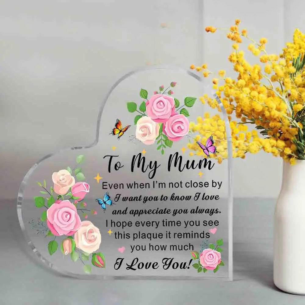 Heart-shaped plaque with floral design and message to 'My Mum' next to a vase of yellow flowers.