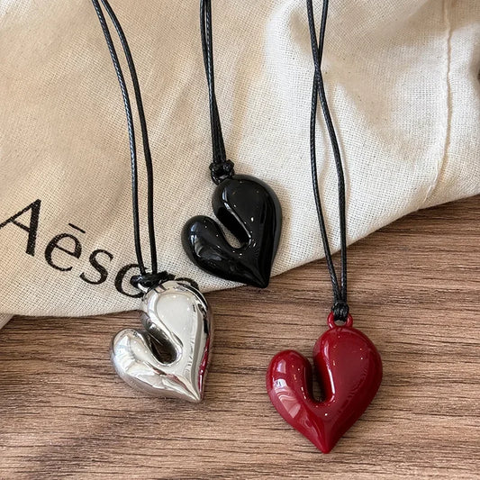 Three heart-shaped pendants on black cords with a beige cloth background