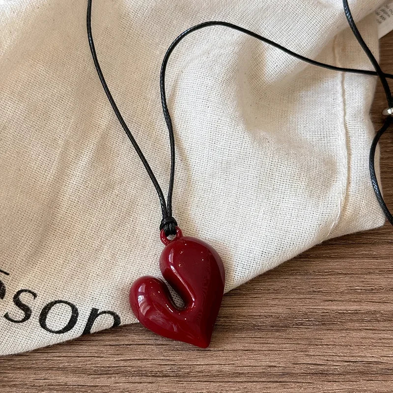 Red heart-shaped pendant on a black cord against a beige fabric background
