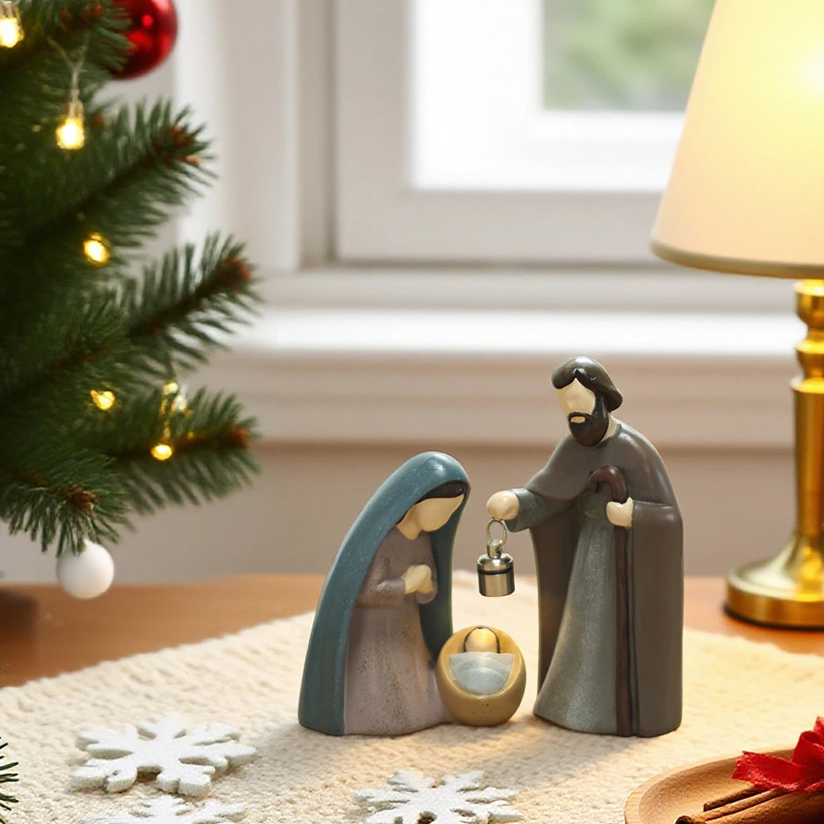 Nativity scene figurines on a table with a Christmas tree and lamp in the background