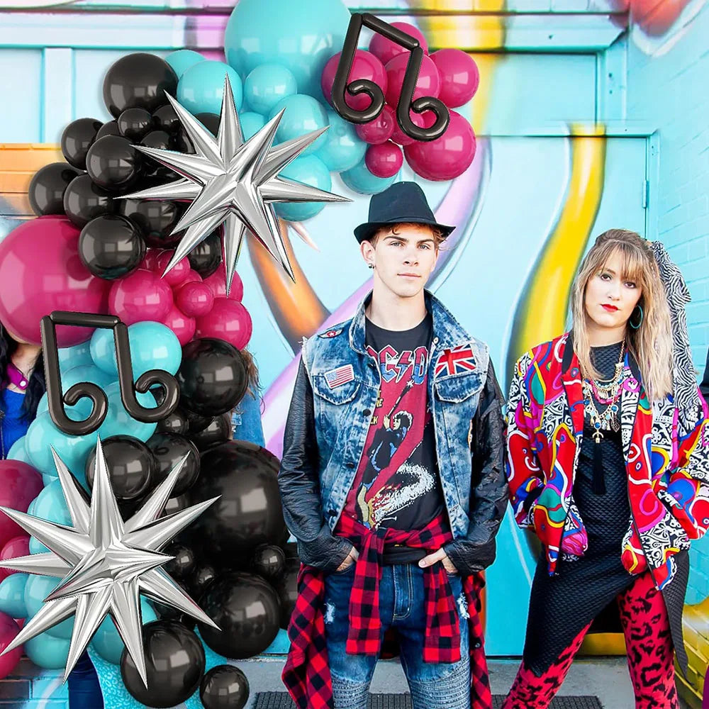 Two people posing in front of a colorful balloon arch with musical notes and numbers.