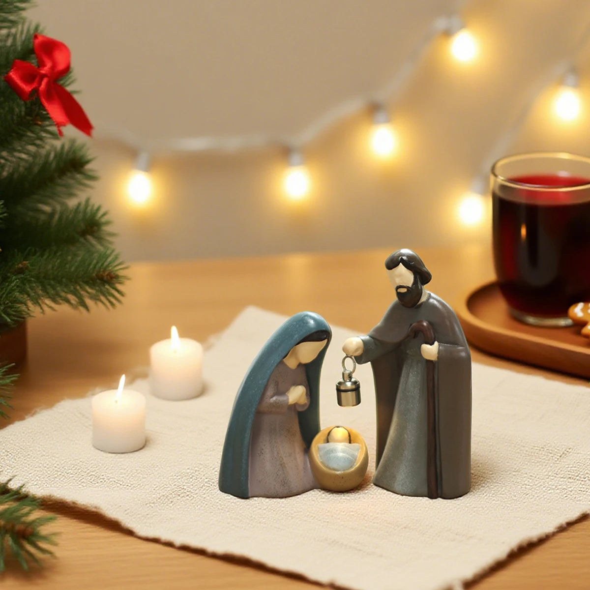Nativity scene figurines on a table with candles and a cup of tea, surrounded by Christmas decorations.