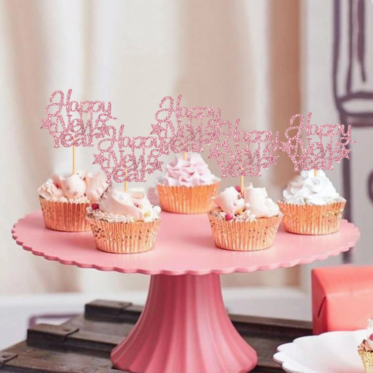 Pink cake stand with cupcakes and 'Happy New Year' toppers on a neutral background