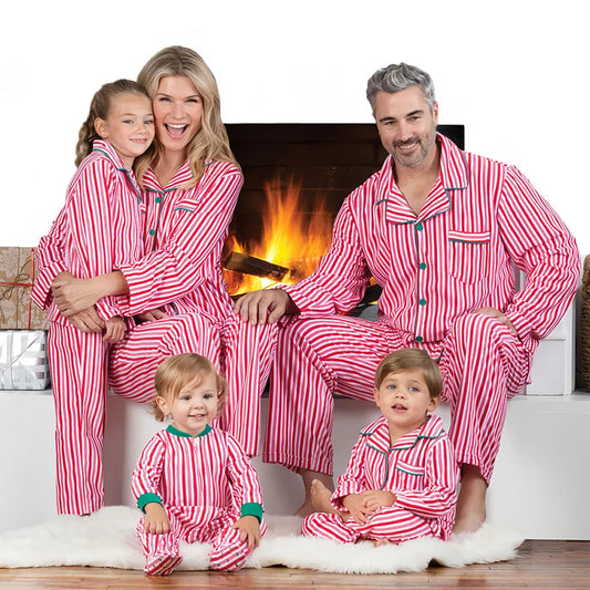 Family of four wearing red and white striped pajamas sitting in front of a fireplace.