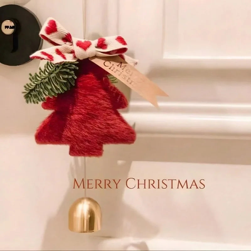 A festive Christmas door ornament featuring a plush red bell-shaped tree, a red and white patterned bow, green pine needles, and a hanging gold bell, shown against a white door with 'MERRY CHRISTMAS' text.