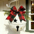A white hanging decorative bell ornament with gold speckles, a black star, and a black handle, decorated with a large red and black buffalo plaid bow, green pine branches, and red berries, hanging on a white exterior wall hook.