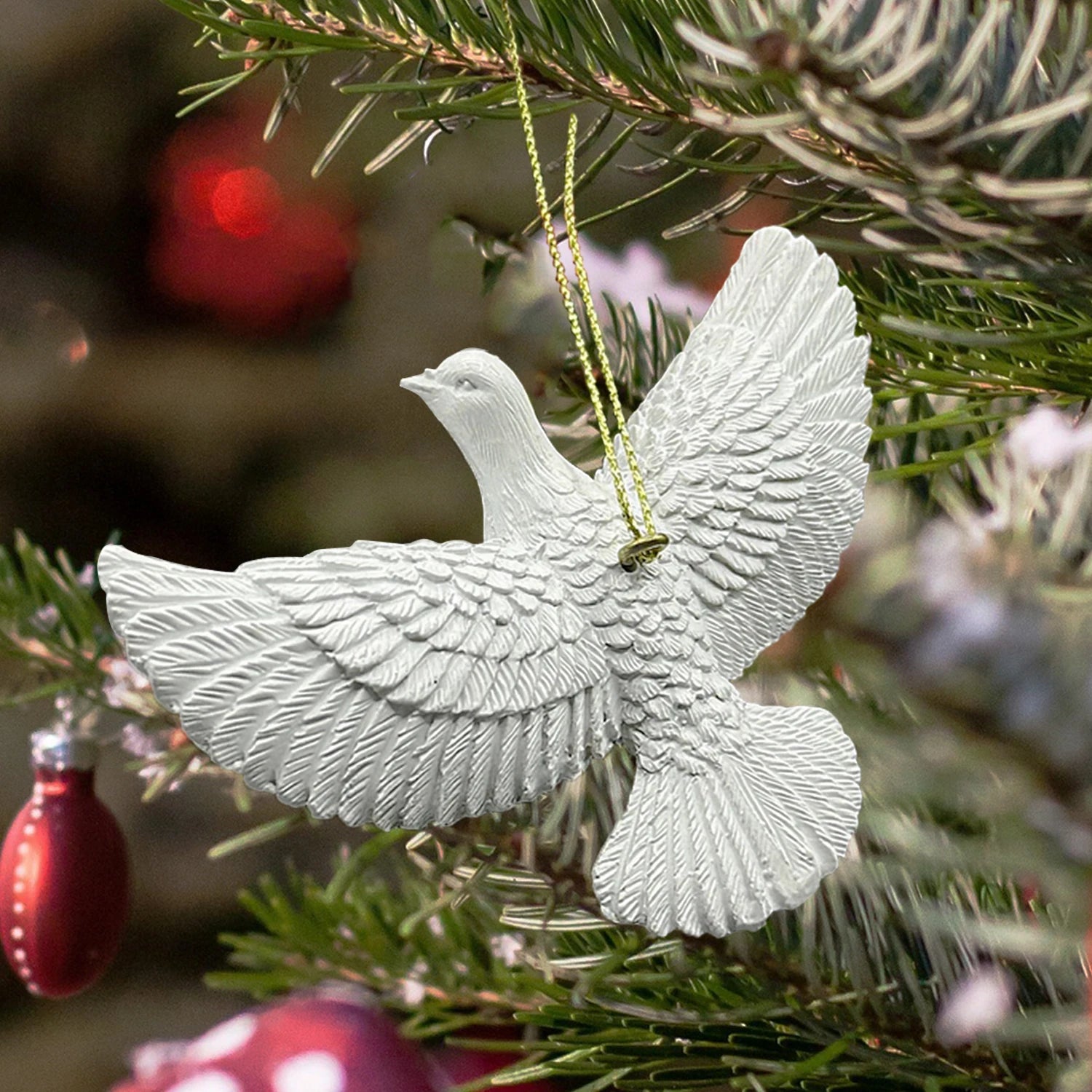 White dove ornament hanging on a Christmas tree with blurred red ornaments in the background.