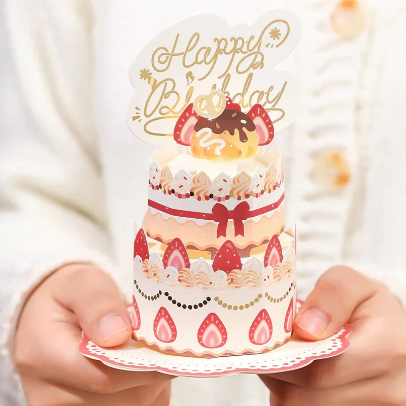 Small card with a birthday cake design and 'Happy Birthday' topper held by hands.