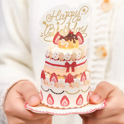 Small card with a birthday cake design and 'Happy Birthday' topper held by hands.