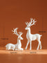 Two white deer figurines with measurements on an orange background