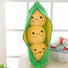 Plush toy shaped like a pod with three smiling yellow avocados inside, on a light surface with a window in the background.